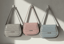 Three quilted flap shoulder bags hanging on wall hooks in grey, blush pink, and powder blue with gold hardware.